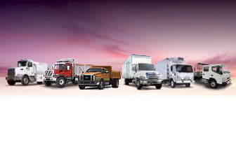 Line up of commercial semi trucks on pink background