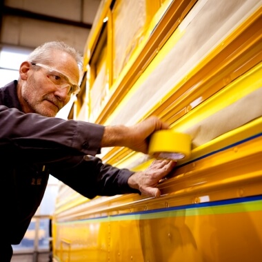Body shop technician applying tape to yellow school bus