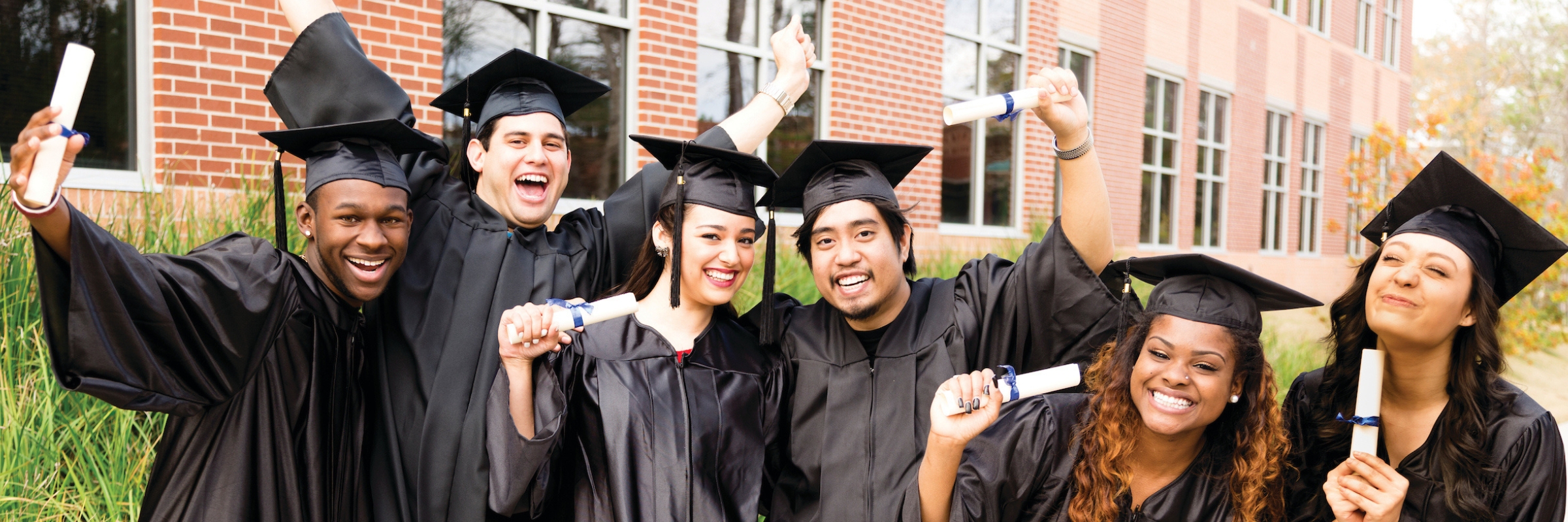 graduates in graduation gowns holding diplomas